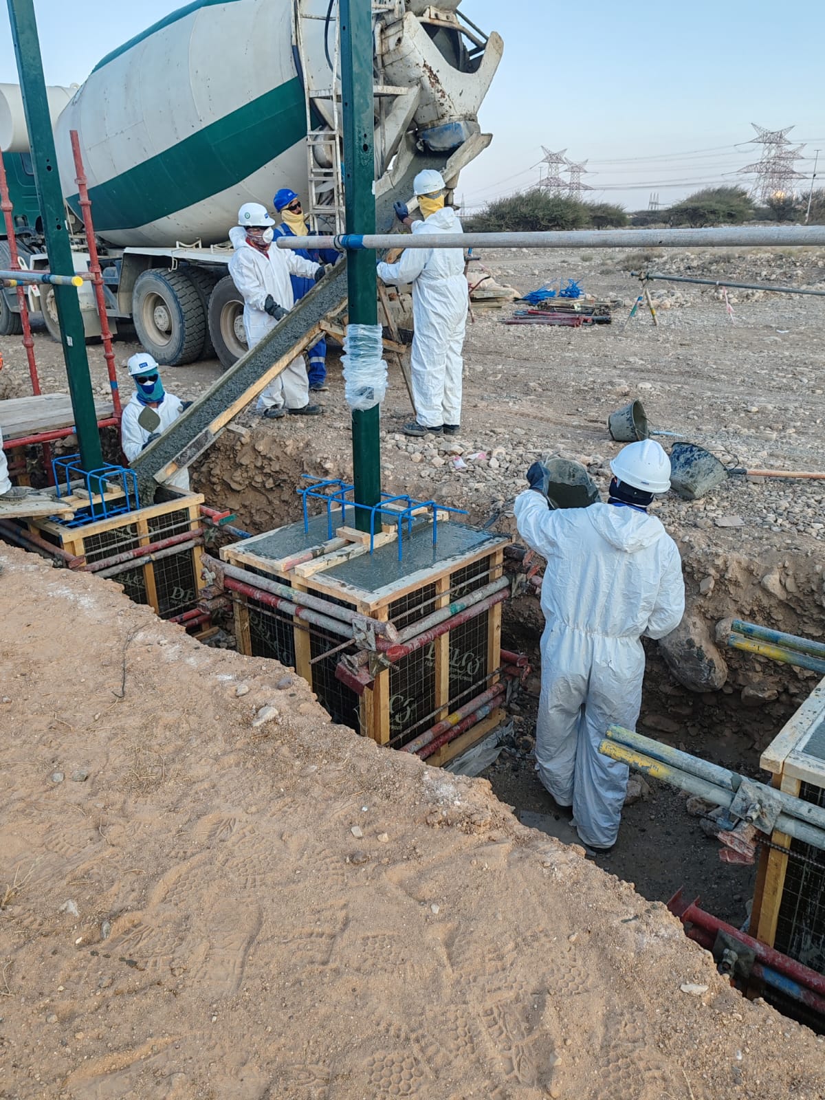 Road construction in oil field with pipelines and facilities in background.